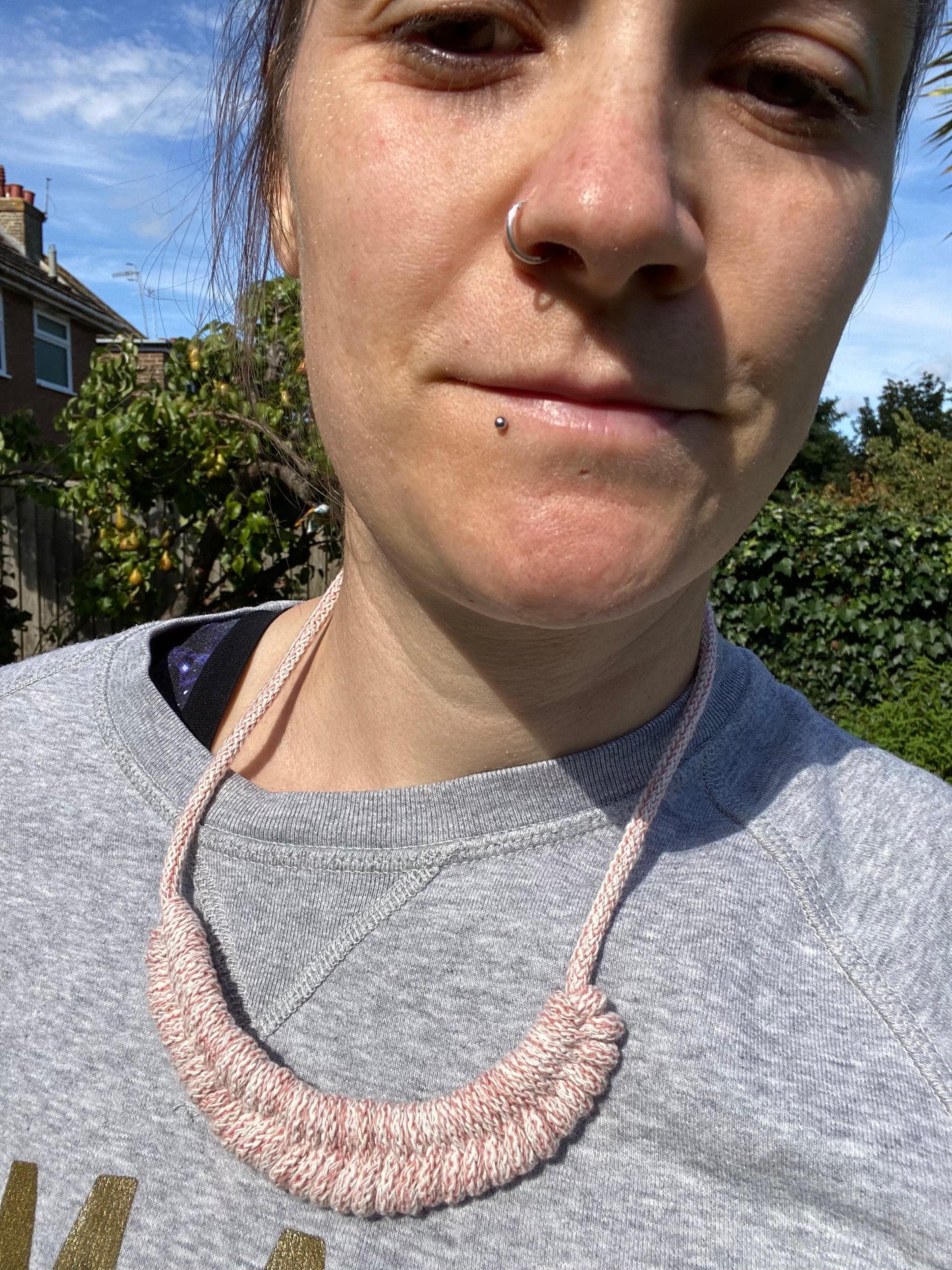 Person wearing a pink necklace outdoors with trees and sky in the background