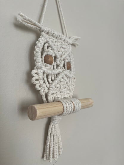 Close up of a handmade macrame owl wall hanging decoration, perched on a wooden dowel. Made with recycled cotton and wooden beads. 