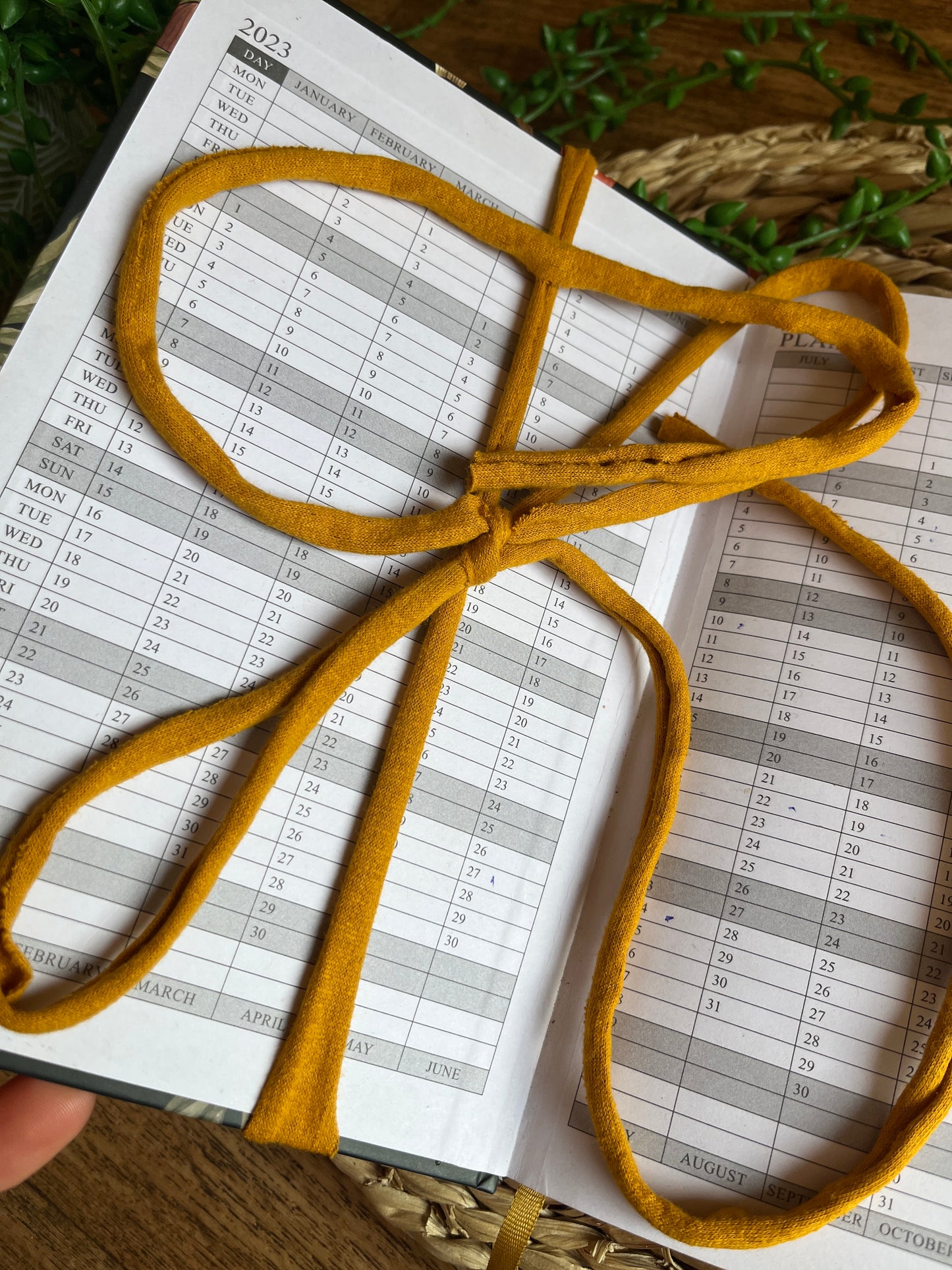 Handmade macrame wrap around pen holder, displayed on a 2023 diary. The image shows the diary open on the first page and shows the yarn wrapped around the page, securing the notebook. 
