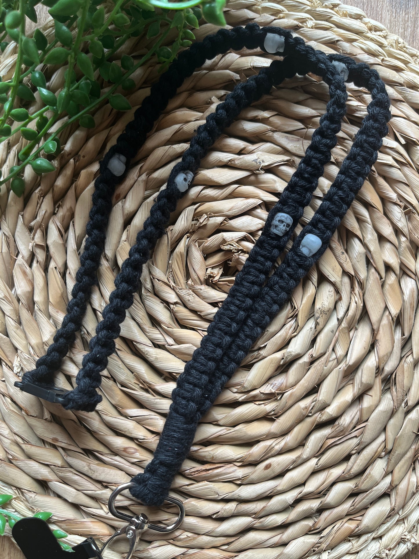 A macrame phone holder lanyard made with black yarn and small skull beads on a wicker mat. 