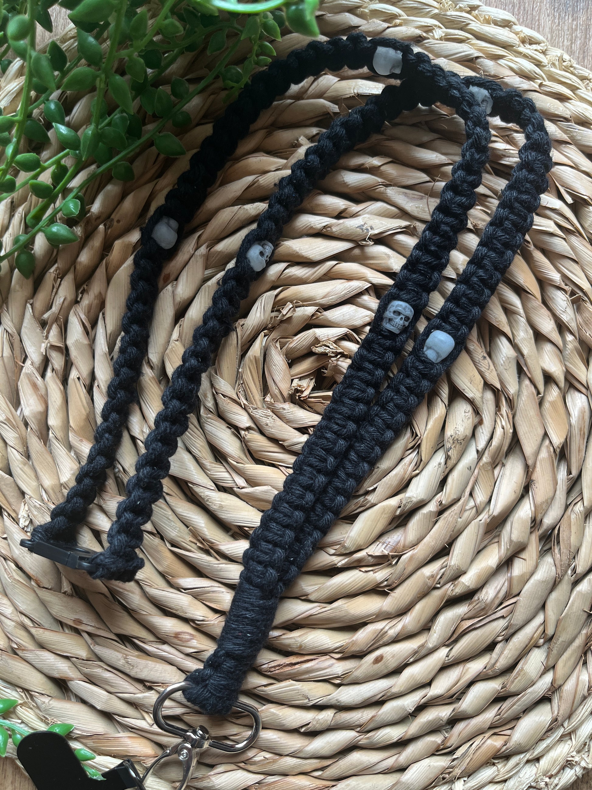 A macrame phone holder lanyard made with black yarn and small skull beads on a wicker mat. 