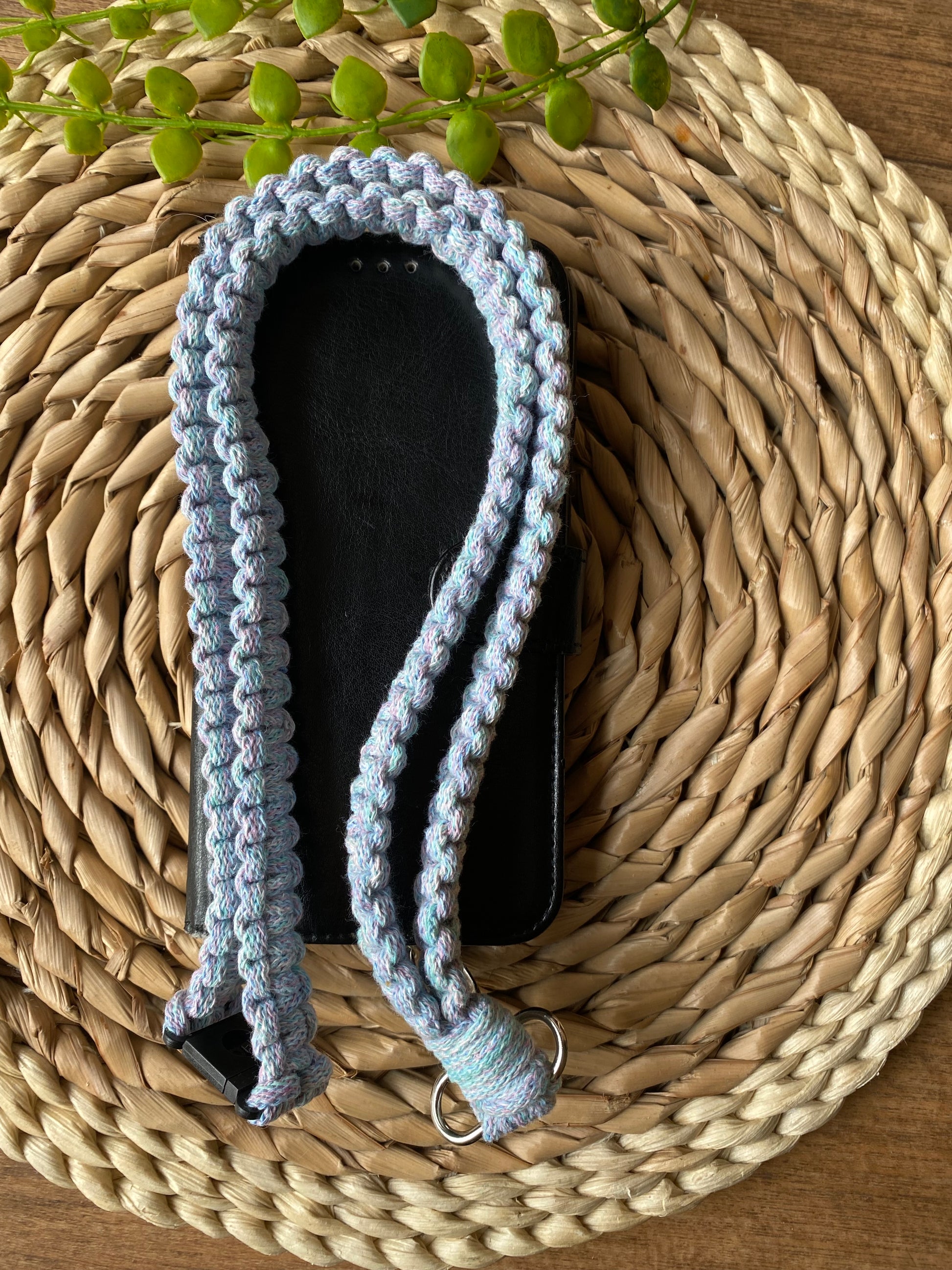A phone case on a wicker mat with a macrame phone lanyard made with pastel coloured yarn folded on top of it. 