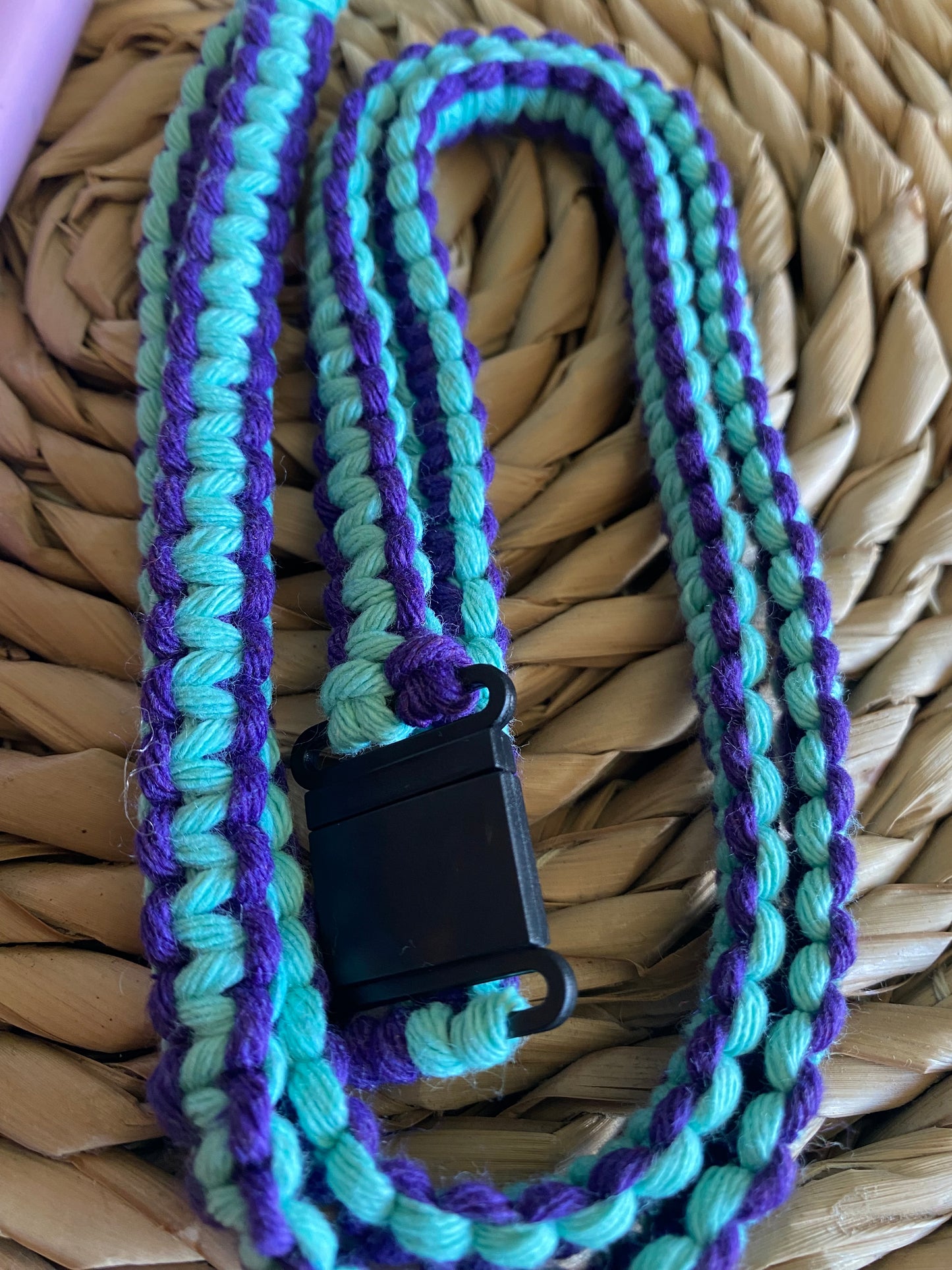 Close up of a macrame phone lanyard made with purple and mint yarn with a black plastic safety break clasp. 