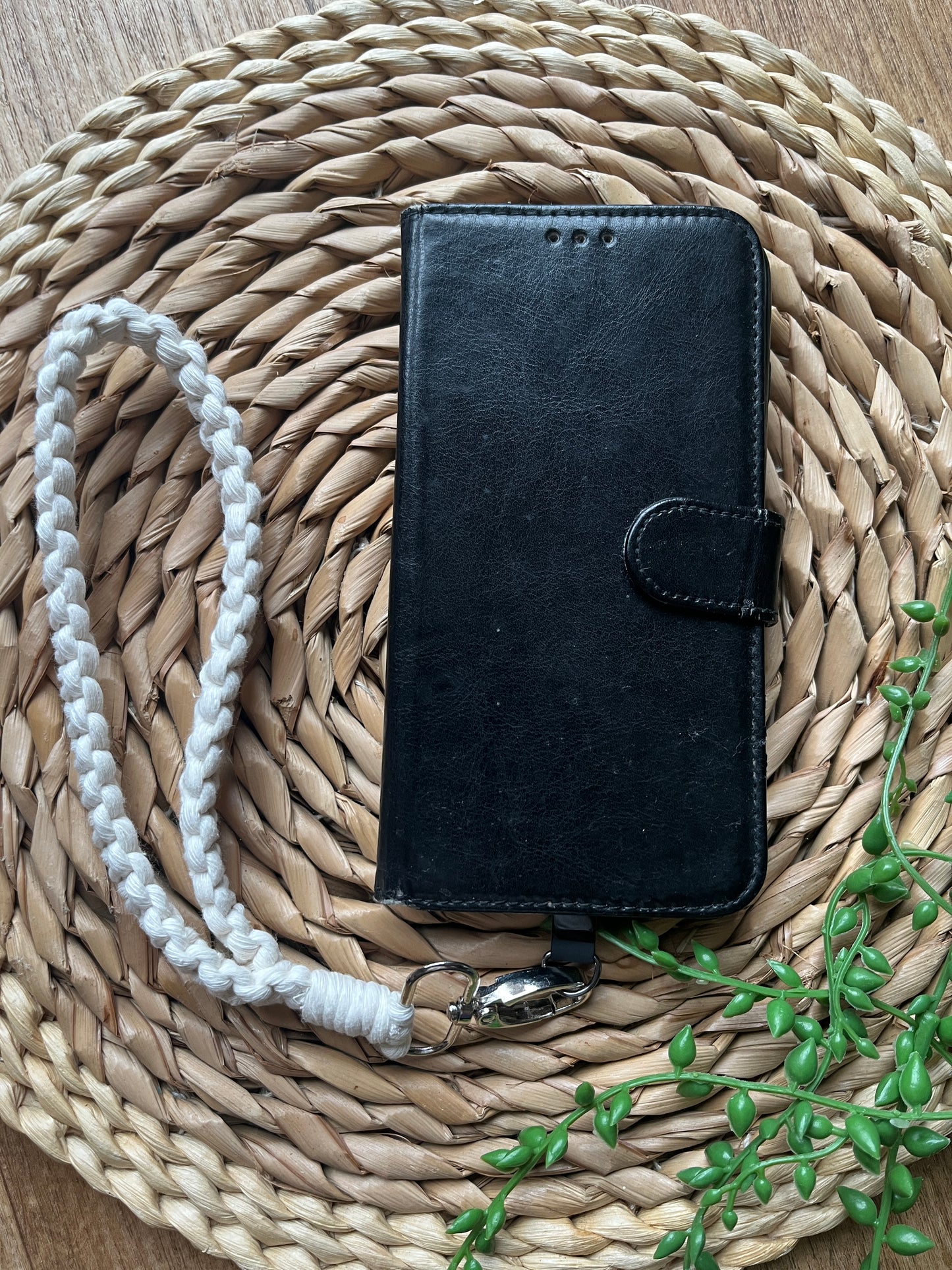 Black leather phone case, with a natural wristlet strap attached with a metal clasp. 