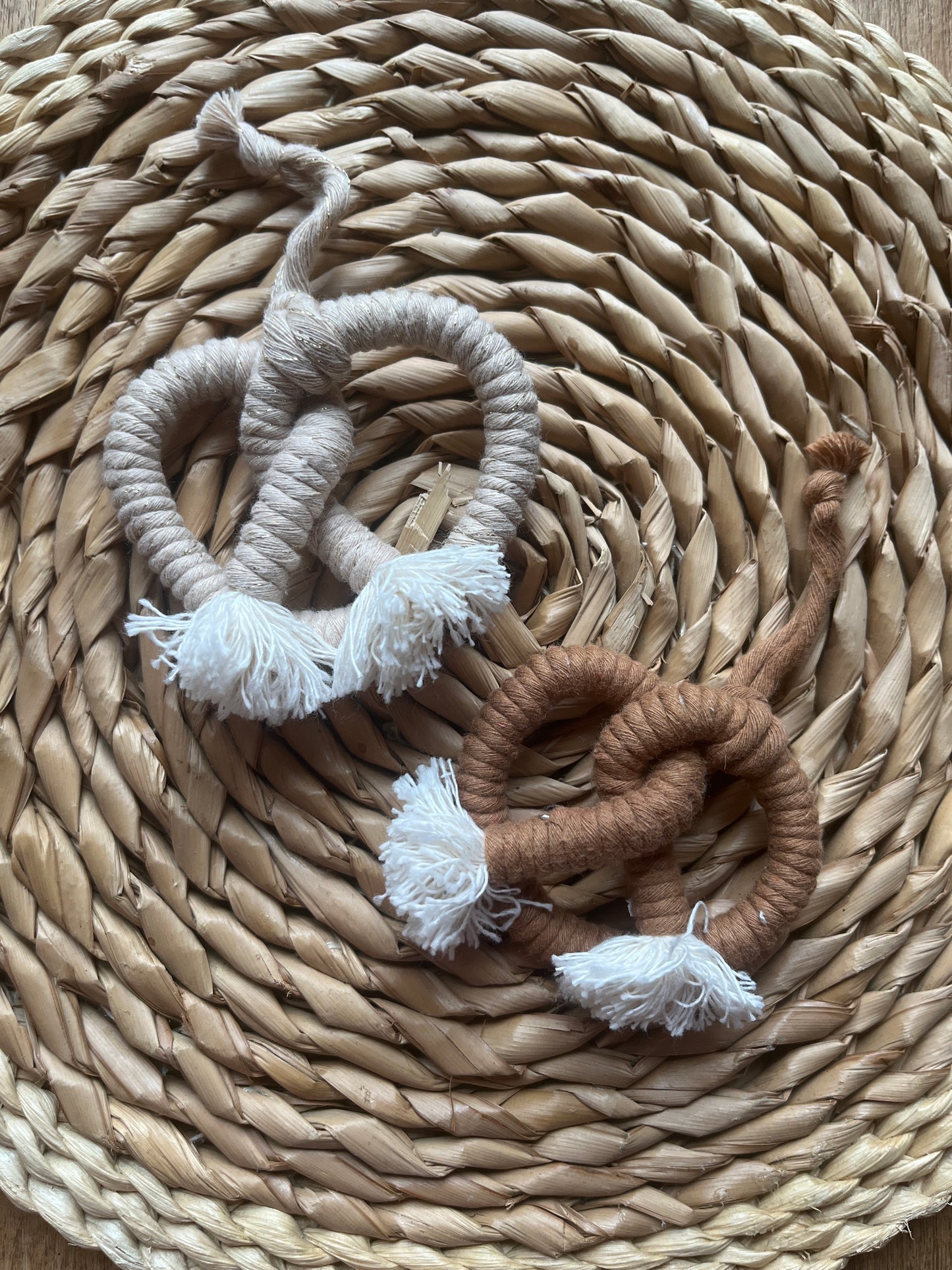 Two macrame rope pretzels, one brown and one beige, on a woven mat.