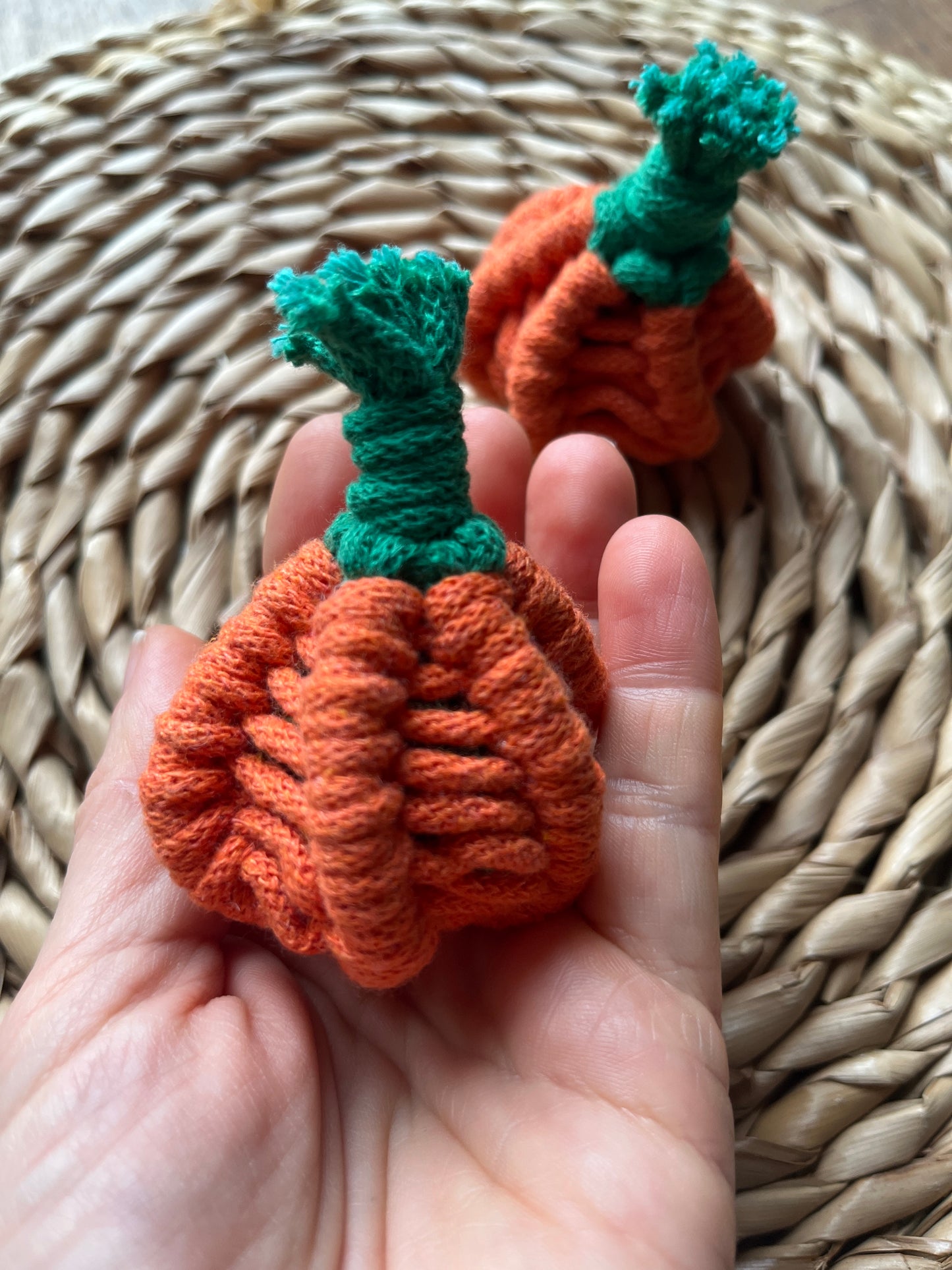 Hand holding a small macrame orange pumpkin with green stem against a woven background