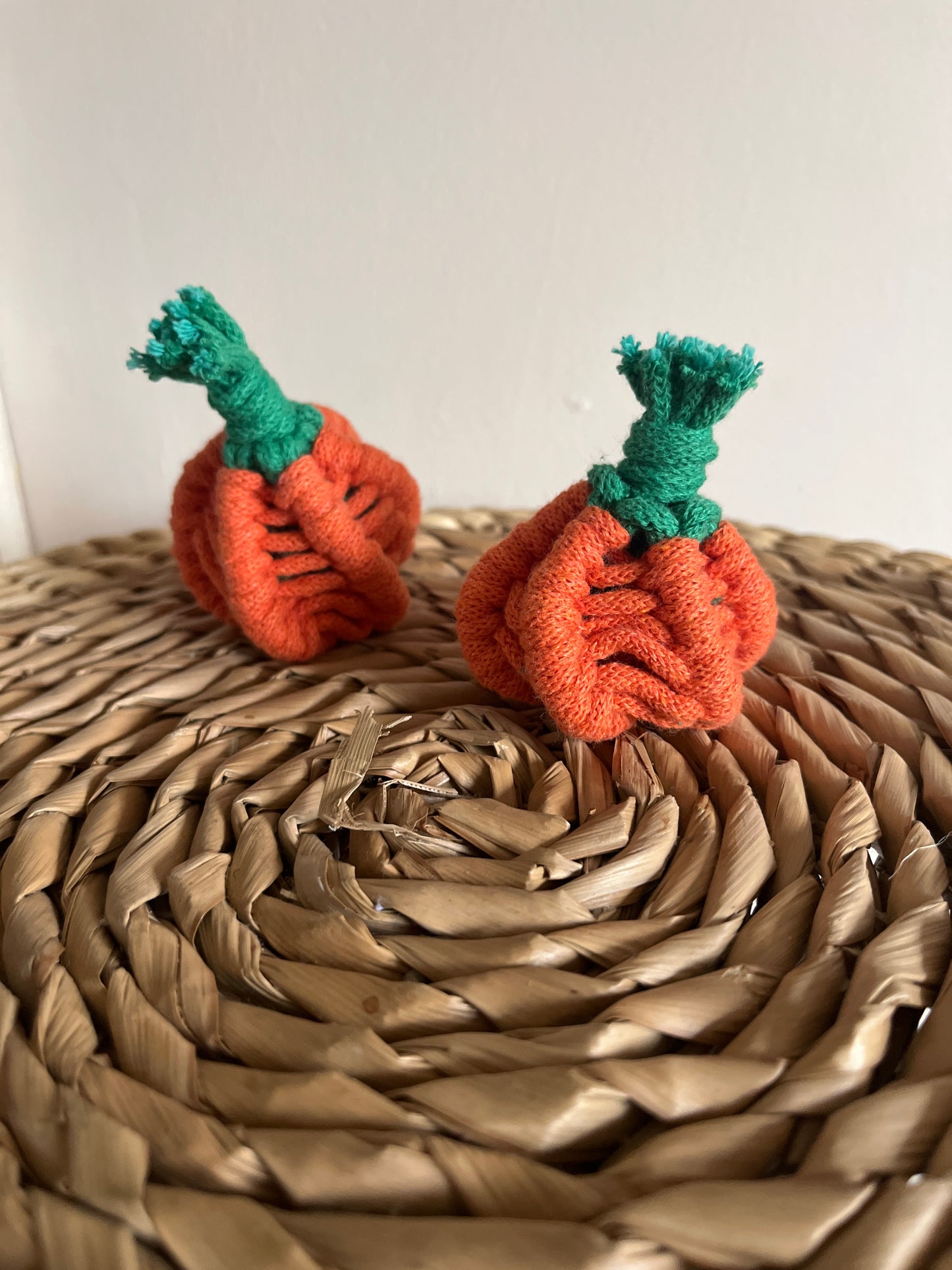 Two macrame pumpkins with green stems on a woven mat.