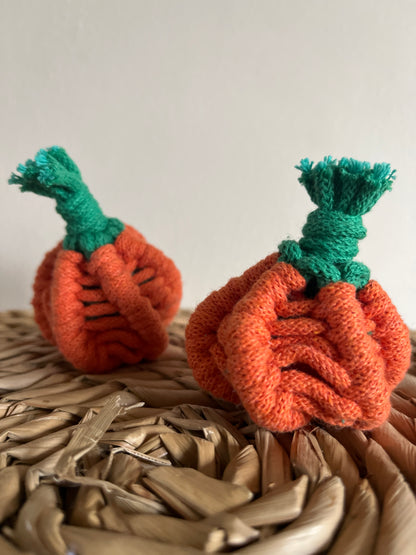 Two macrame pumpkins with green stems on a woven mat against a white background
