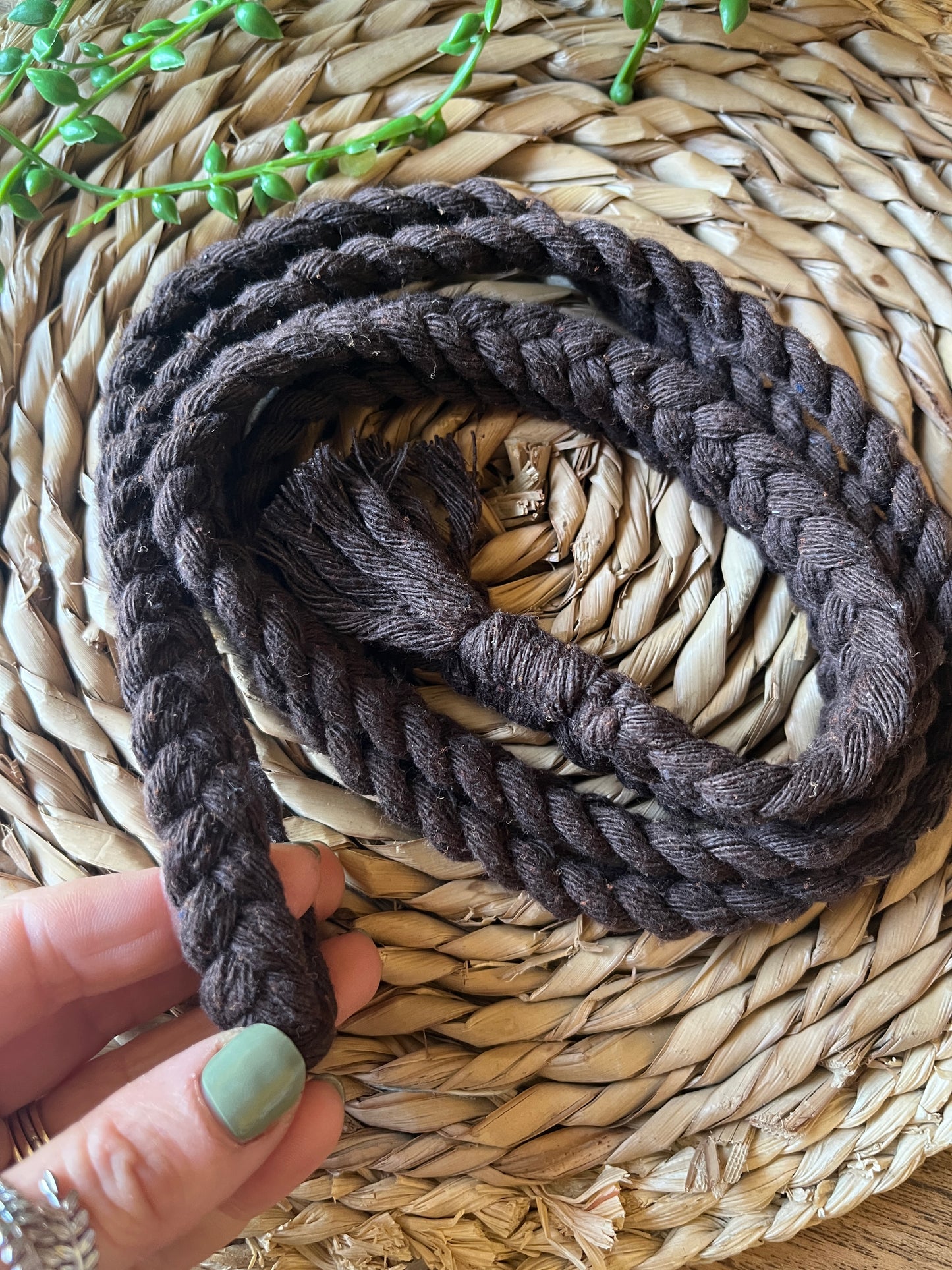 A hands holding a coiled brown cotton rope belt on a round wicker surface. 
