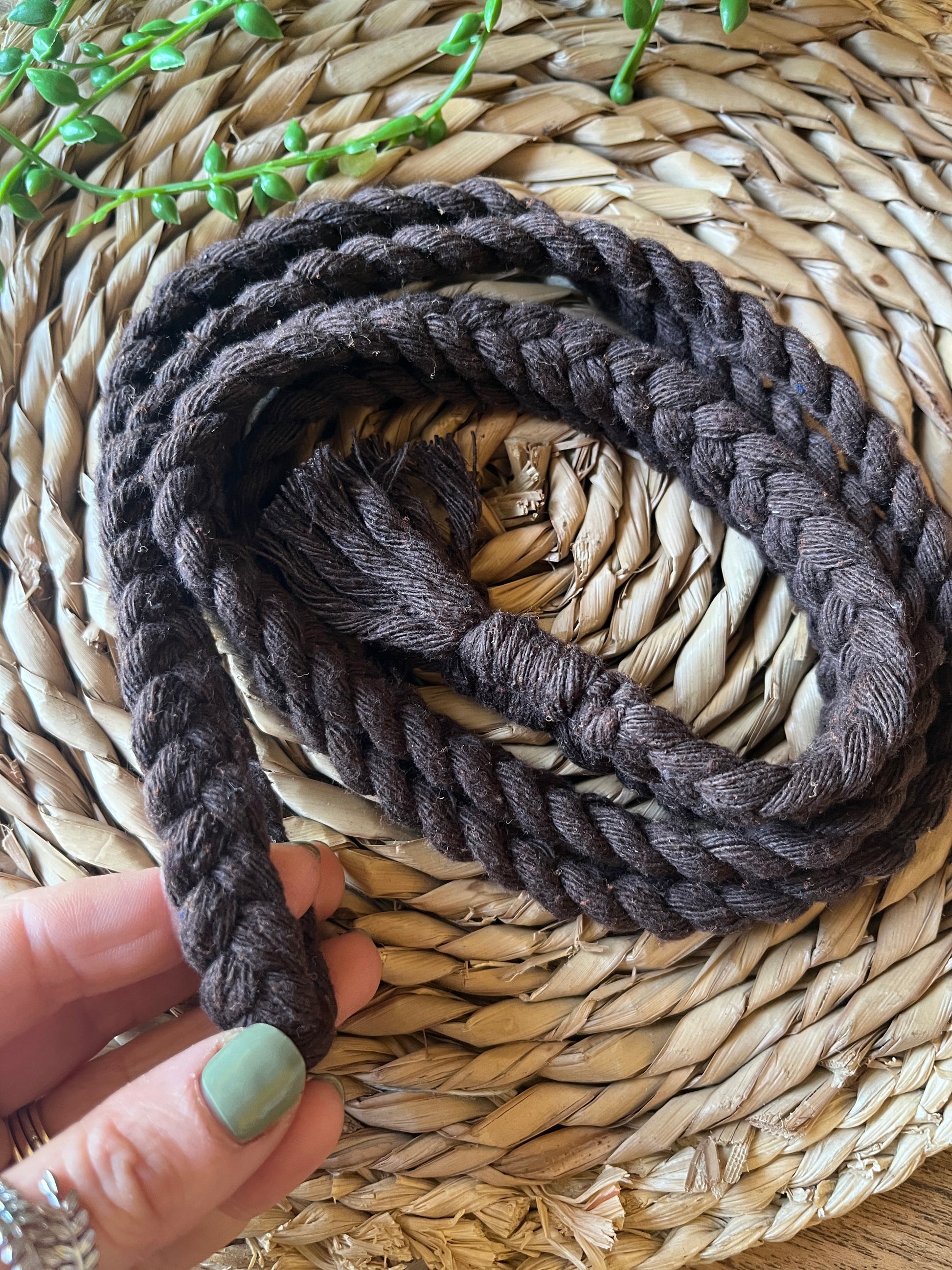A hands holding a coiled brown cotton rope belt on a round wicker surface. 