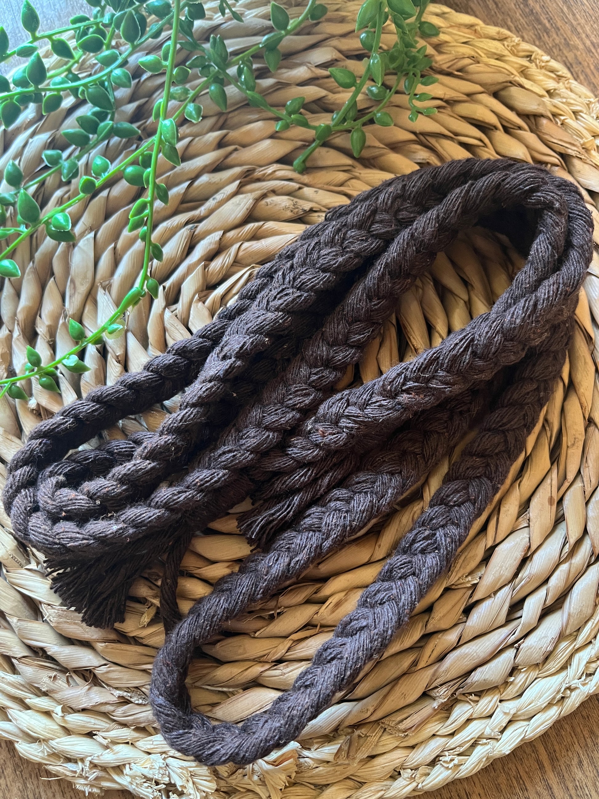A coiled brown braided cotton macrame rope belt rests on a round wicker surface. 