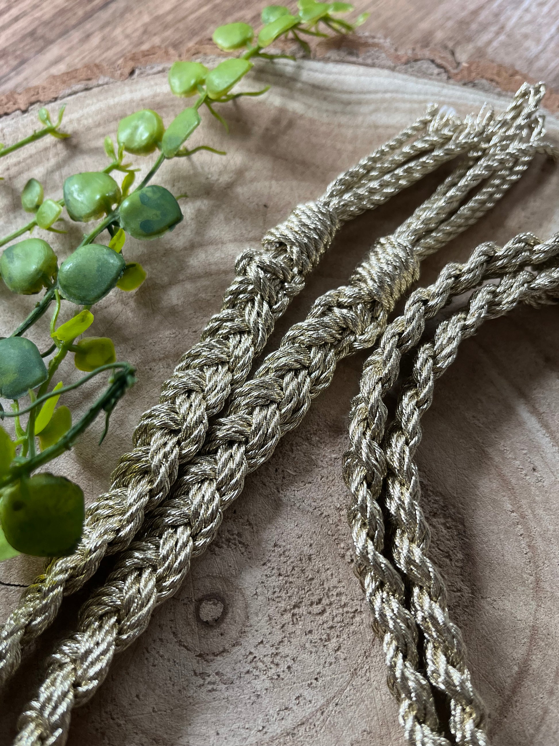 A gold braided macrame rope belt rests on a round wooden surface. 