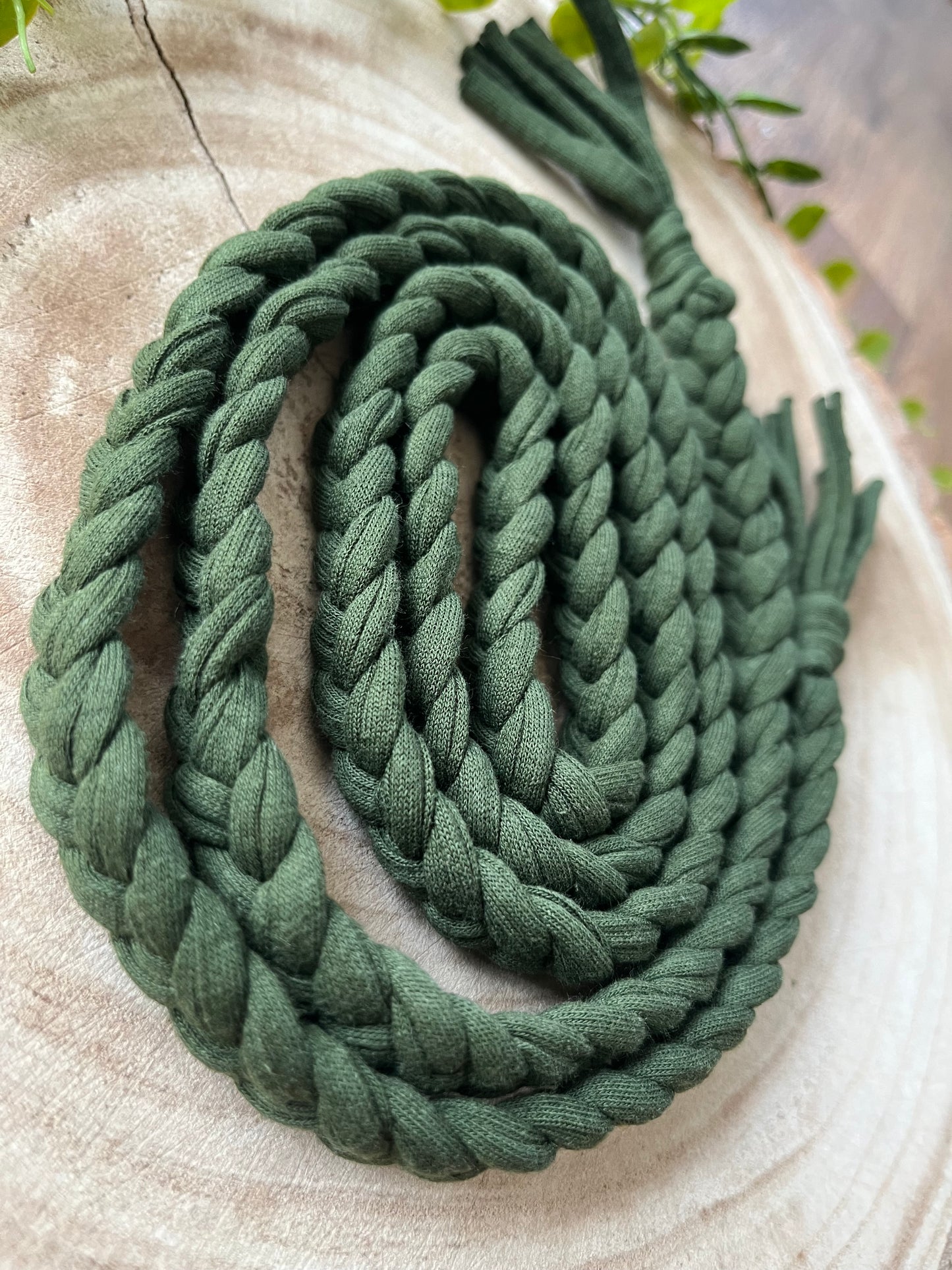 A coiled green t shirt yarn belt rests on a round wooden surface. 