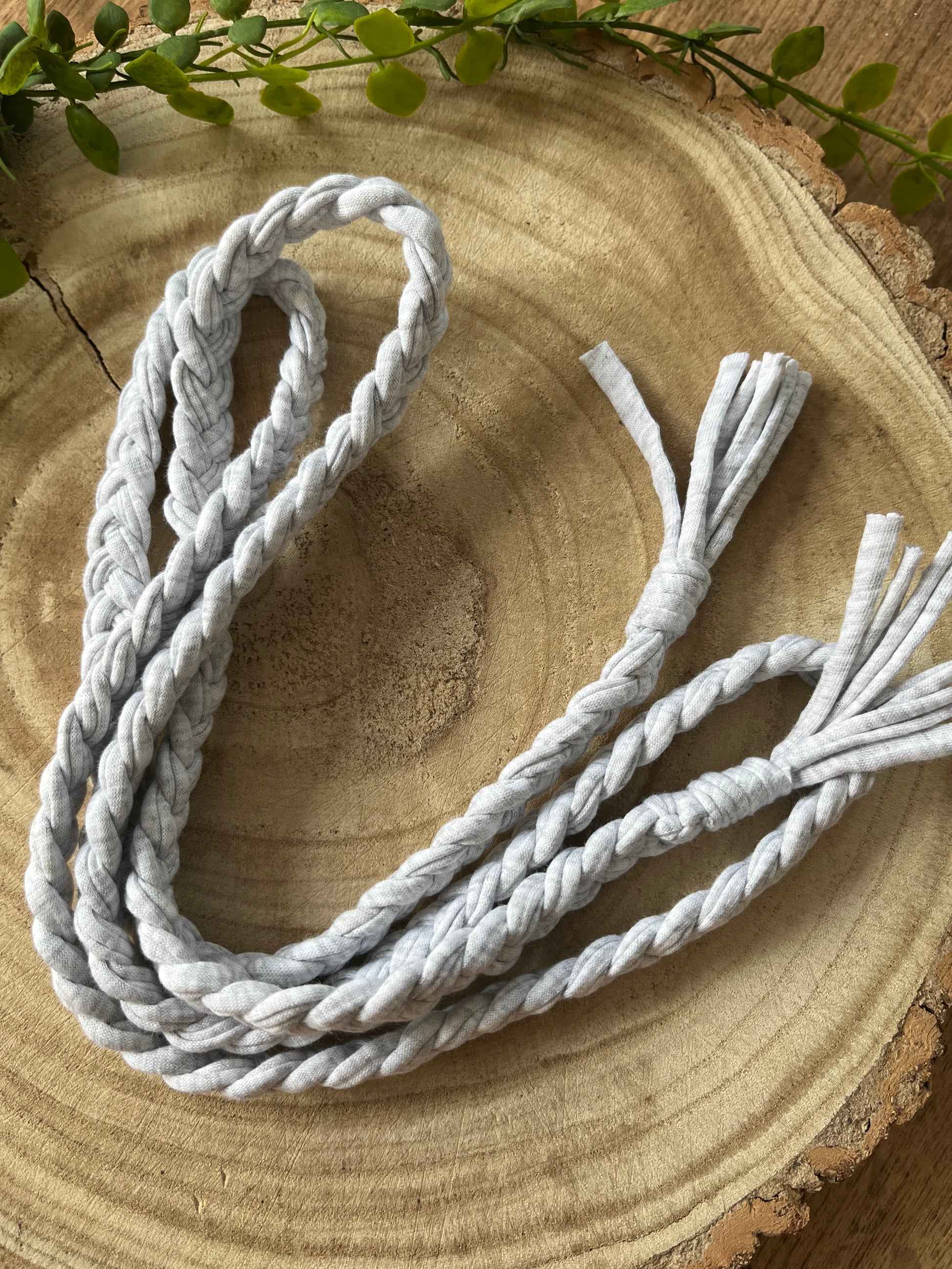 A coiled grey t shirt yarn braided waist belt rests on a round wooden surface. 