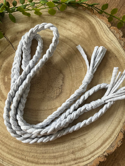 A coiled grey t shirt yarn braided waist belt rests on a round wooden surface. 