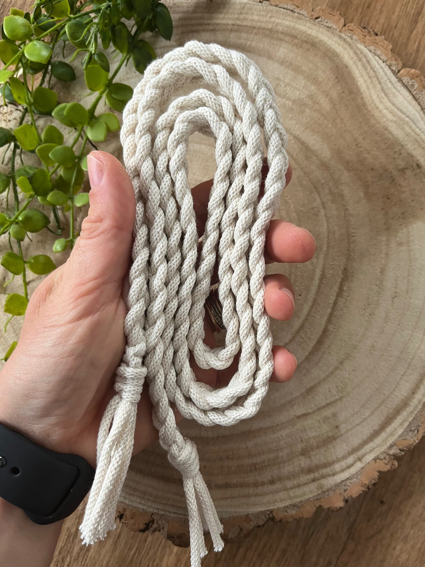 A hand holds a handmade braided macrame belt made with natural yarn over a wooden surface.