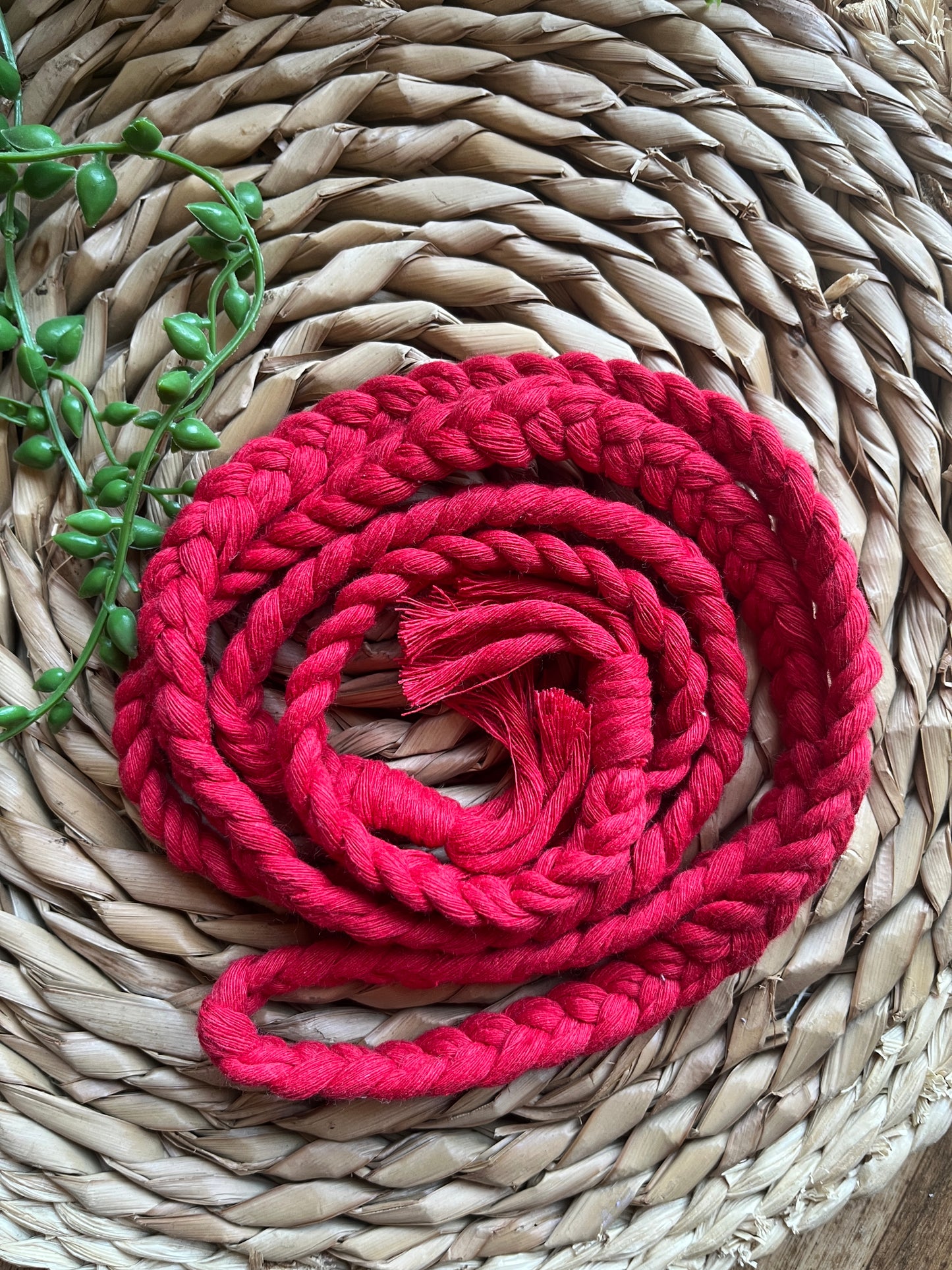 A red braided rope belt laid out on a woven mat, with tasseled ends. 