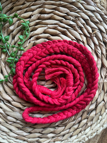 A red braided rope belt laid out on a woven mat, with tasseled ends. 
