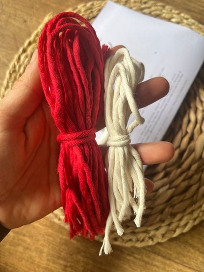 Red and white yarn held by a hand over a woven surface