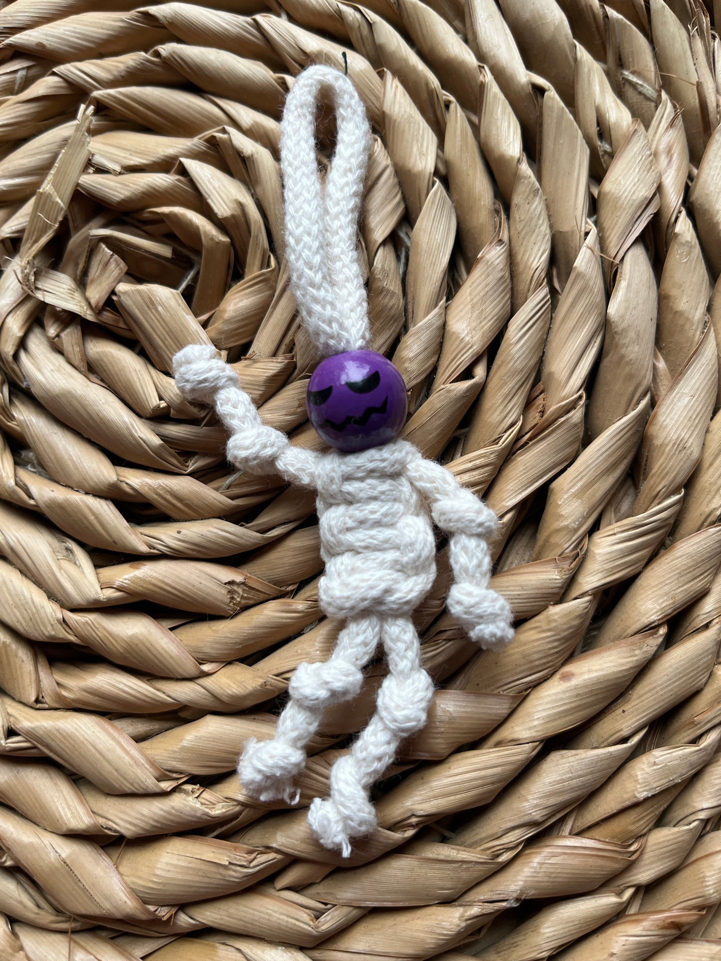 White knotted macrame skeleton with a purple bead on a woven mat