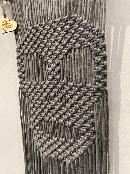 Close up of a dark grey macrame wall hanging with a knotted pattern in the shape of a skull. 