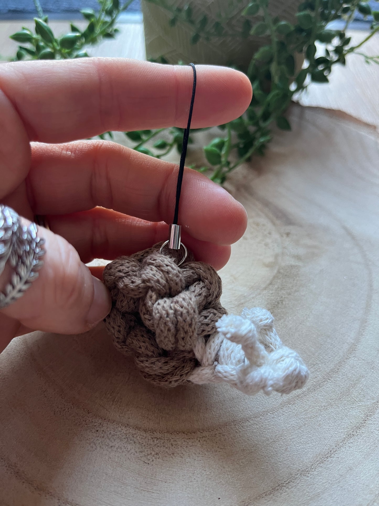 Hand holding a small macrame snail charm, against a wooden background