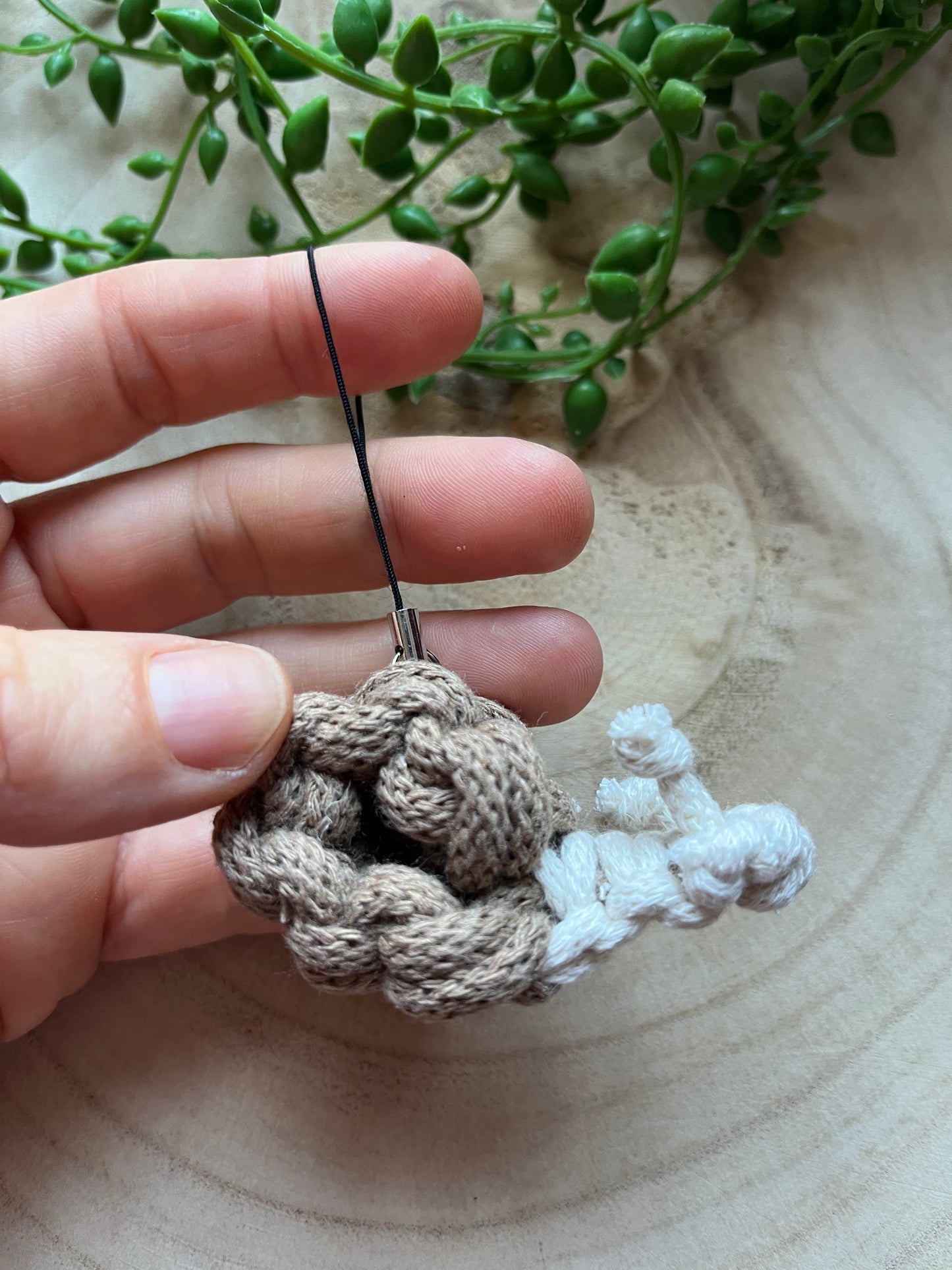 Hand holding a small macrame snail on a wooden surface