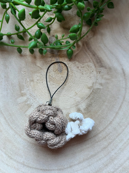 Knotted snail keychain on a wooden surface with a plant