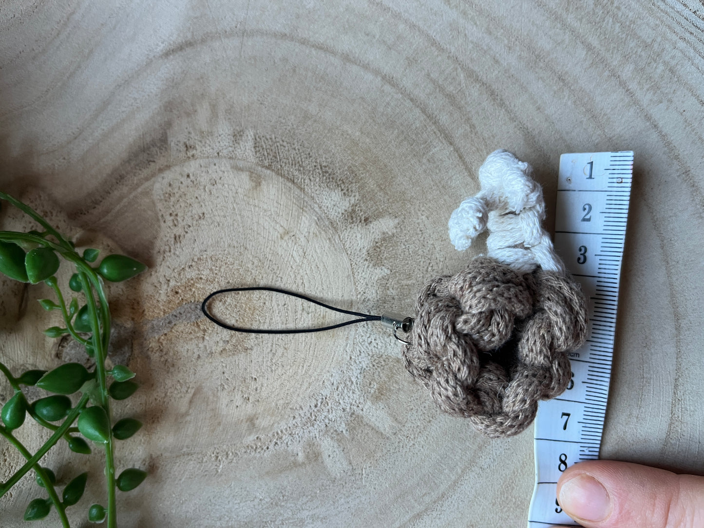 Knotted snail keychain with a measuring tape for scale on a wooden surface.