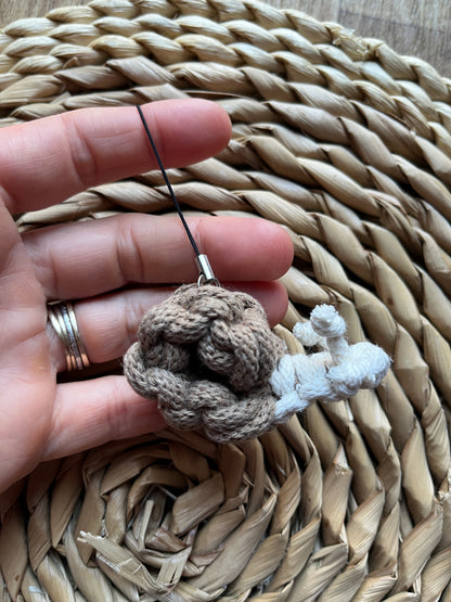 Hand holding a small macrame snail against a woven mat background