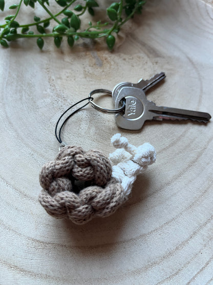 Macrame snail keychain attached to keys on a wooden surface with a plant in the corner