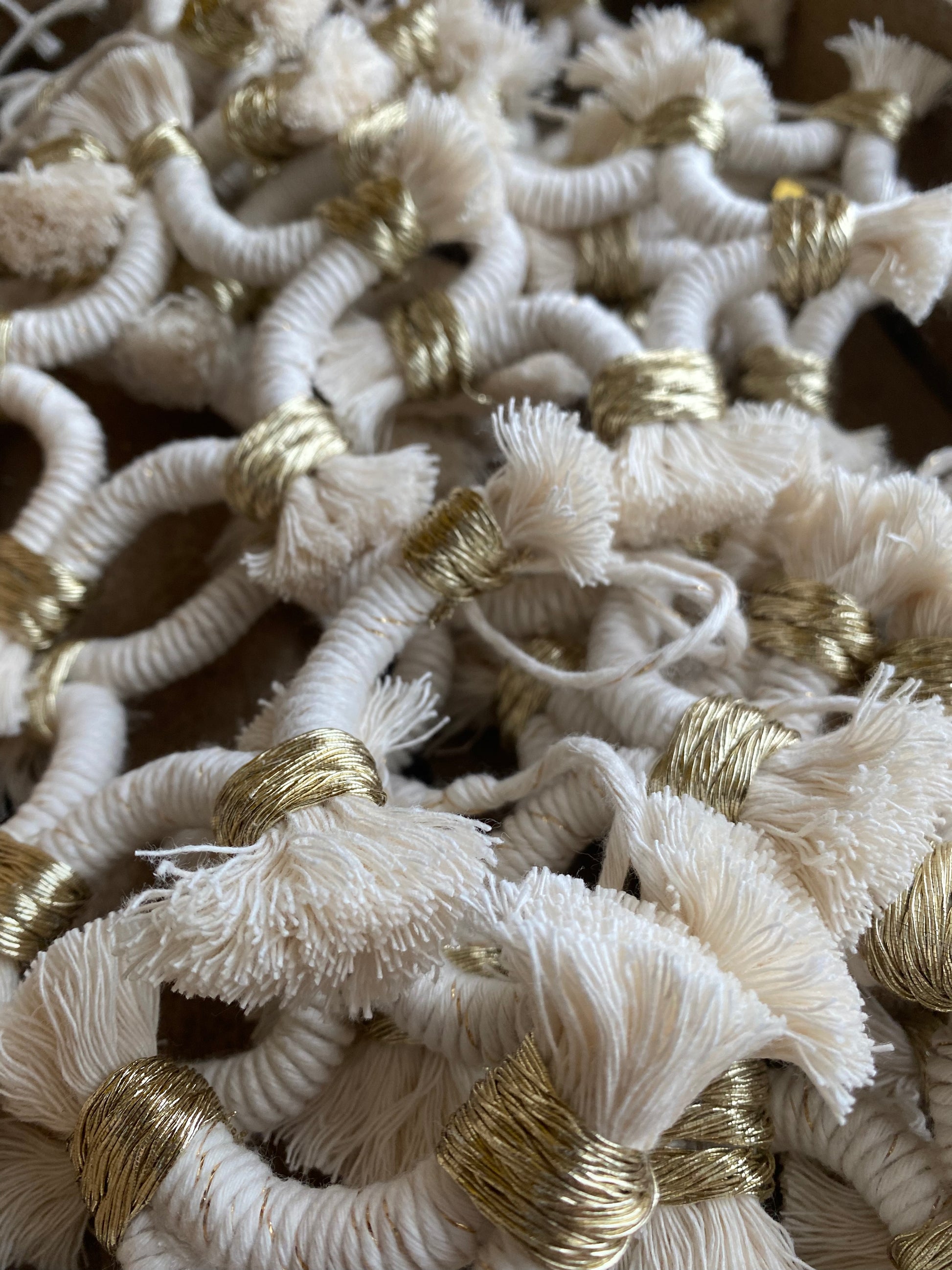 A pile of small macrame star shaped hanging decorations, made with natural yarn with gold detailing, and fringed ends.