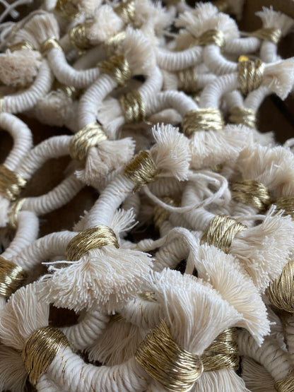 A pile of small macrame star shaped hanging decorations, made with natural yarn with gold detailing, and fringed ends.