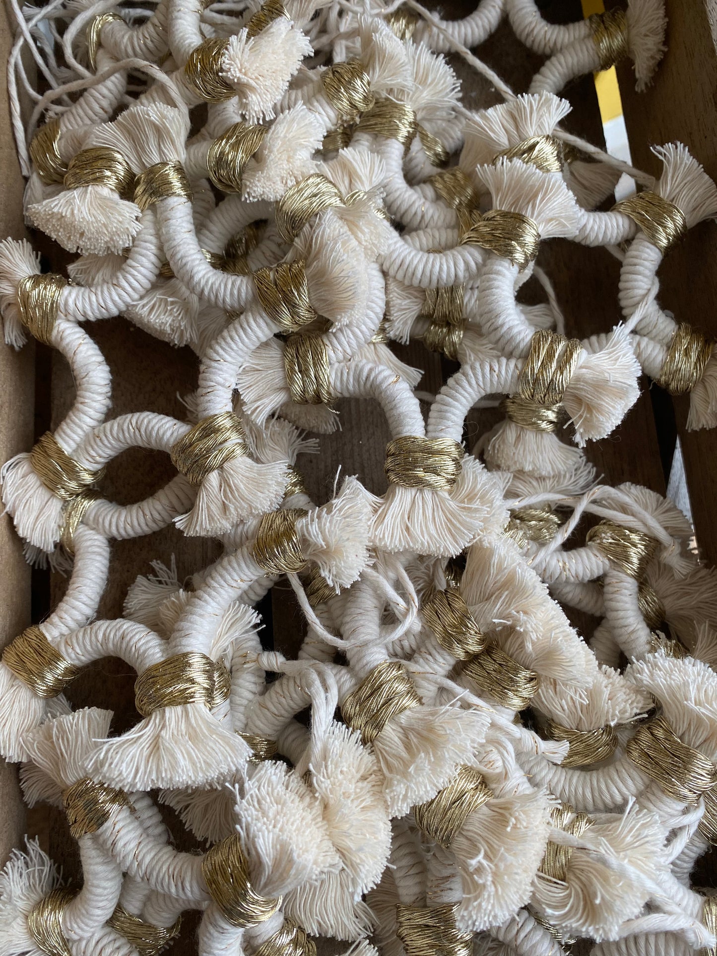 A pile of small macrame star shaped hanging decorations, made with natural yarn with gold detailing, and fringed ends.