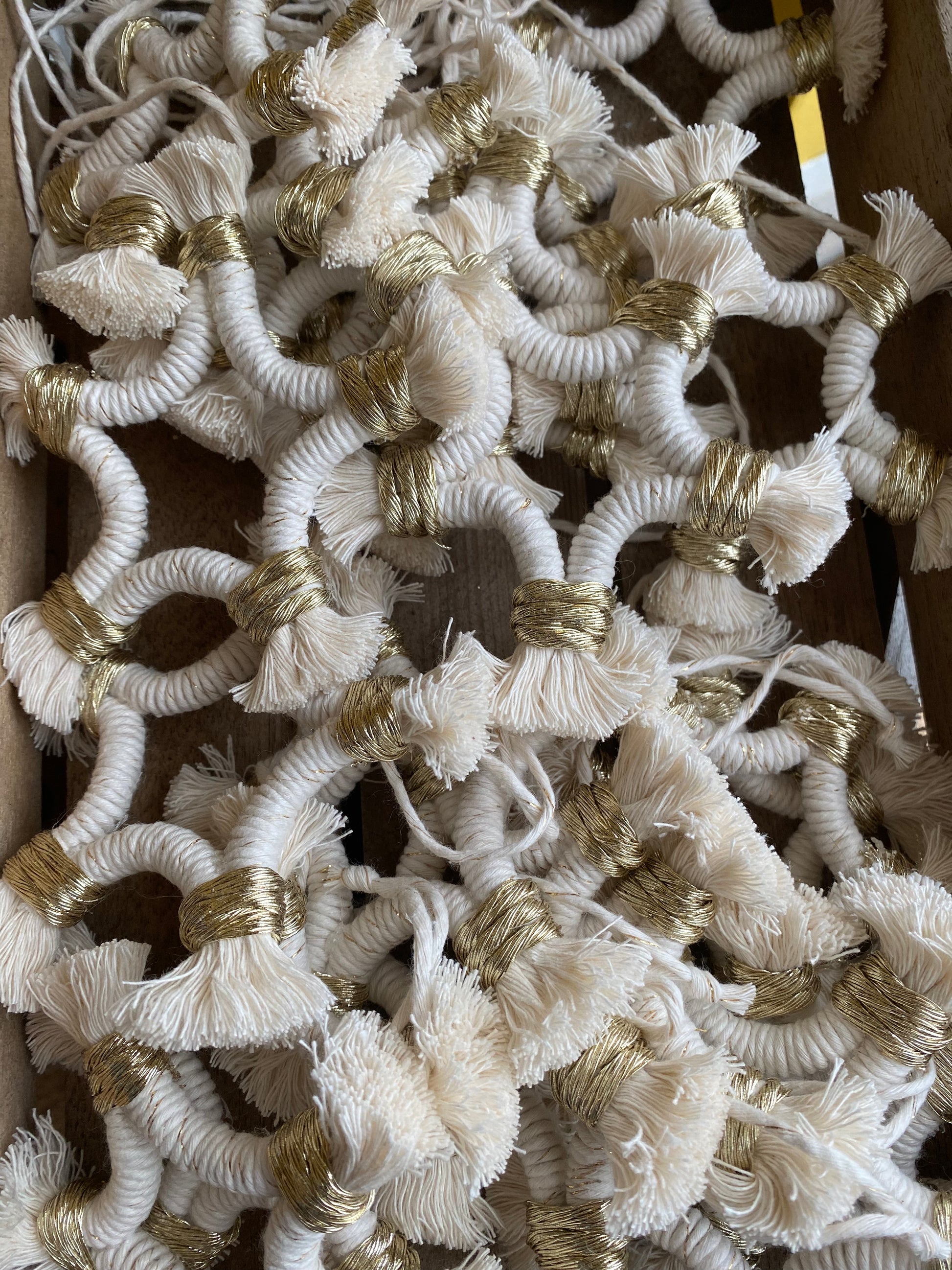 A pile of small macrame star shaped hanging decorations, made with natural yarn with gold detailing, and fringed ends.
