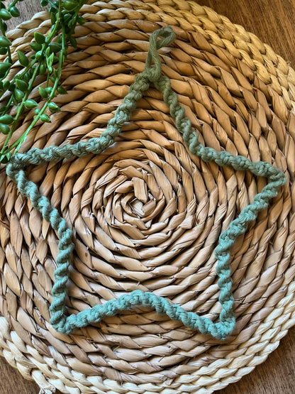 Star shaped wall hanging, wrapped in green cotton with a twisted knot pattern, laid flat on a circular woven mat.
