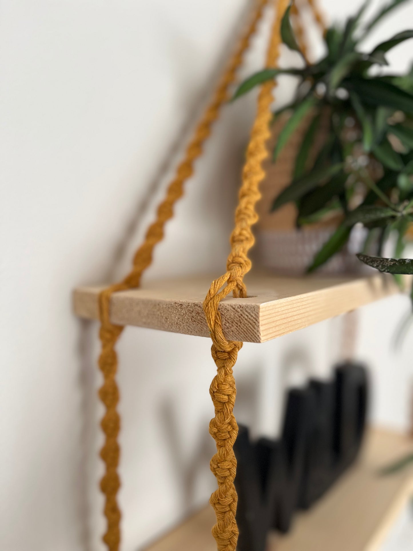 Close up image focusing on the mustard yellow coloured knotted yarn, on a set of macrame wooden shelves. 