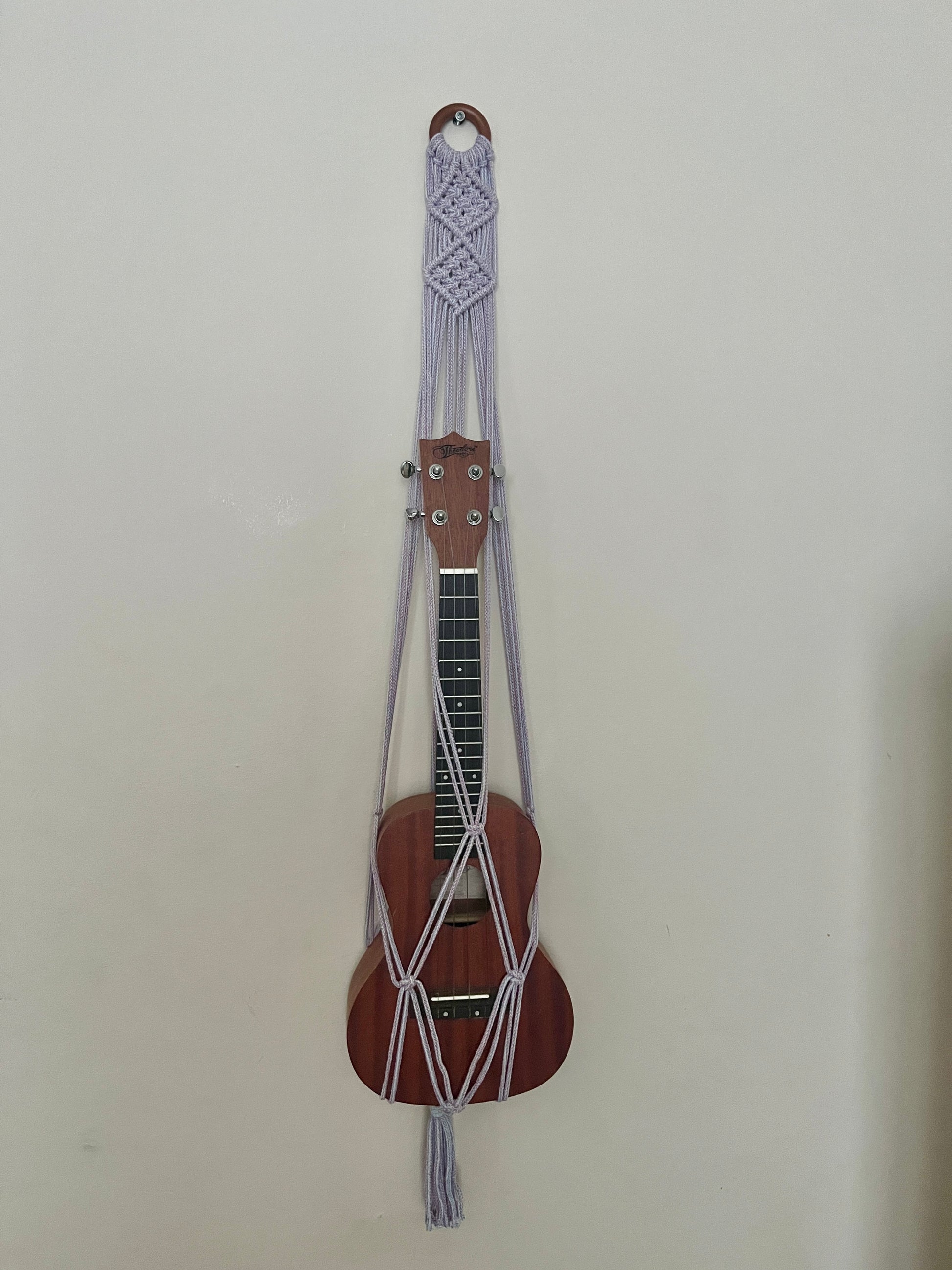Brown ukulele securely held in a macrame strap on a beige background