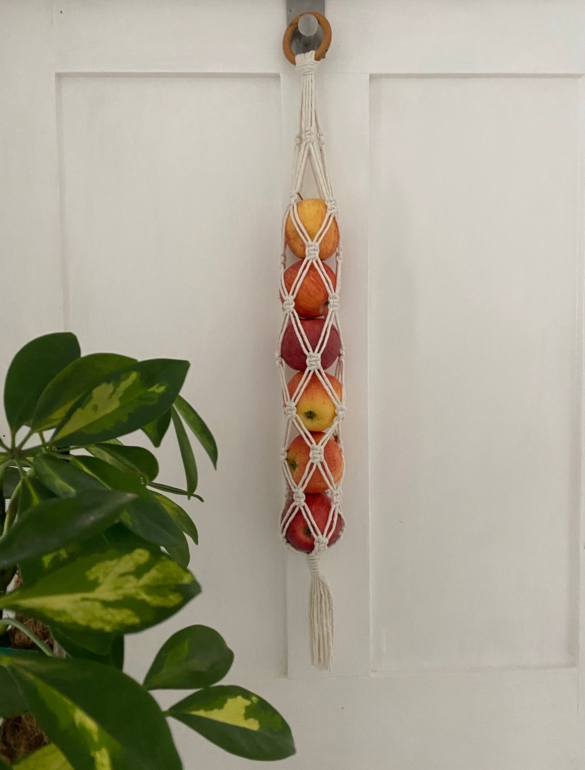 Macrame fruit holder with apples hanging on a white door