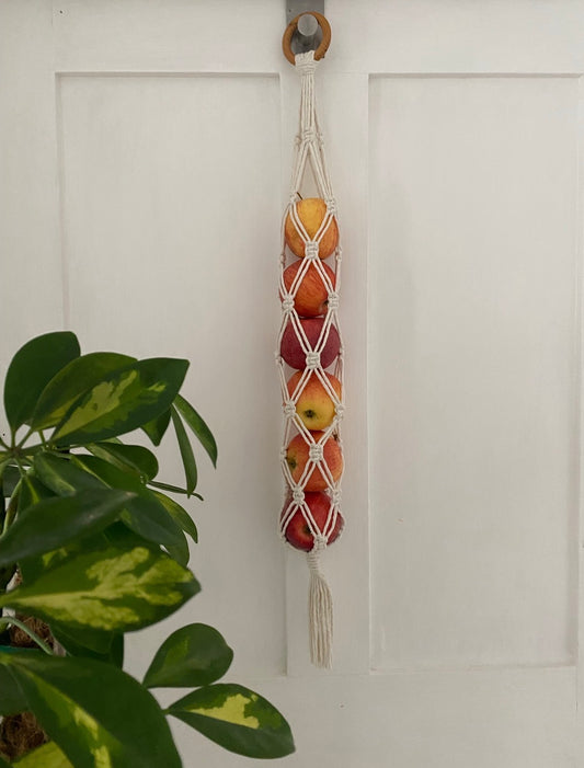 Macrame fruit holder with apples hanging on a white door