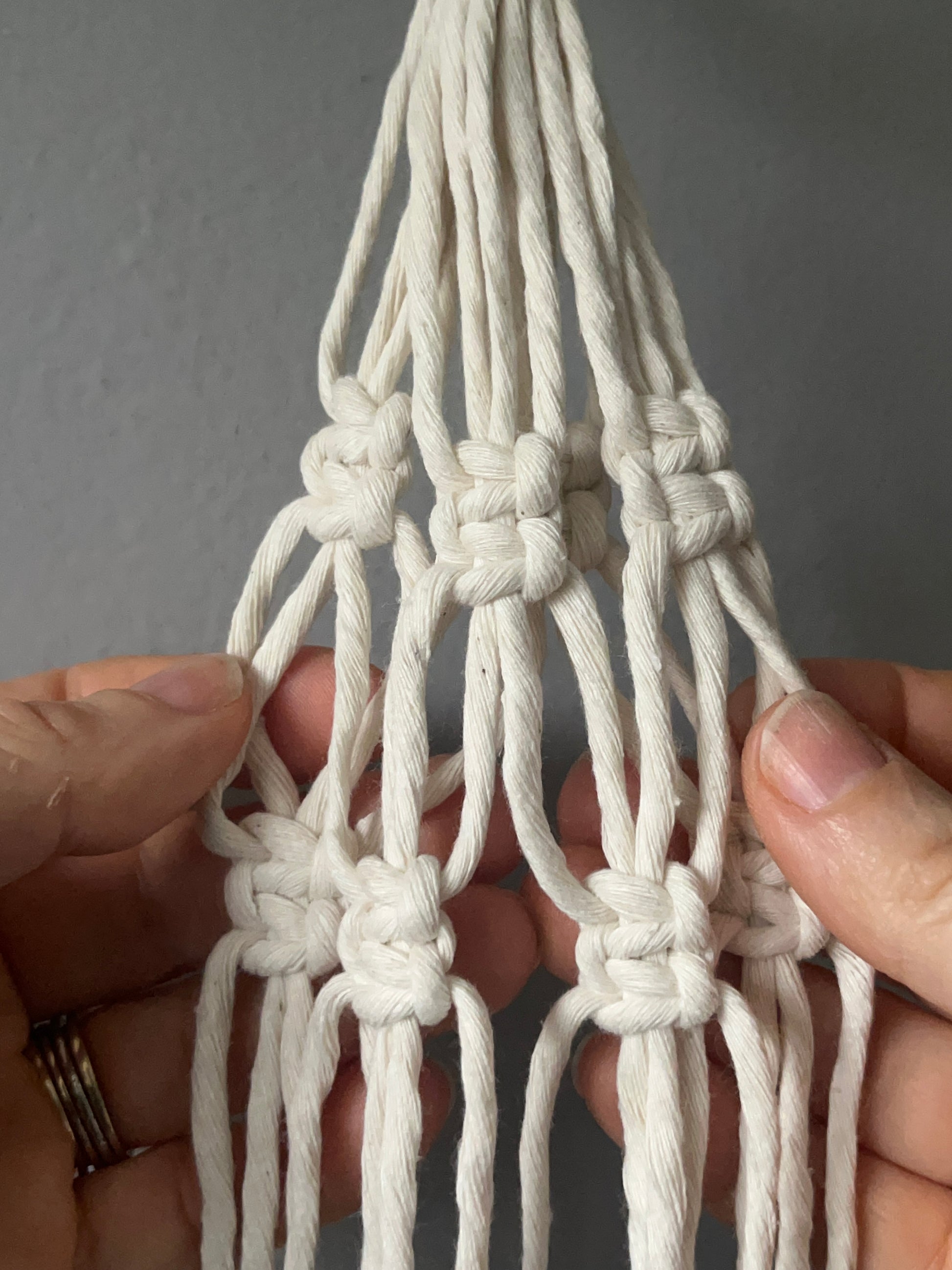 Close-up of hands holding a knotted macrame project against a grey background