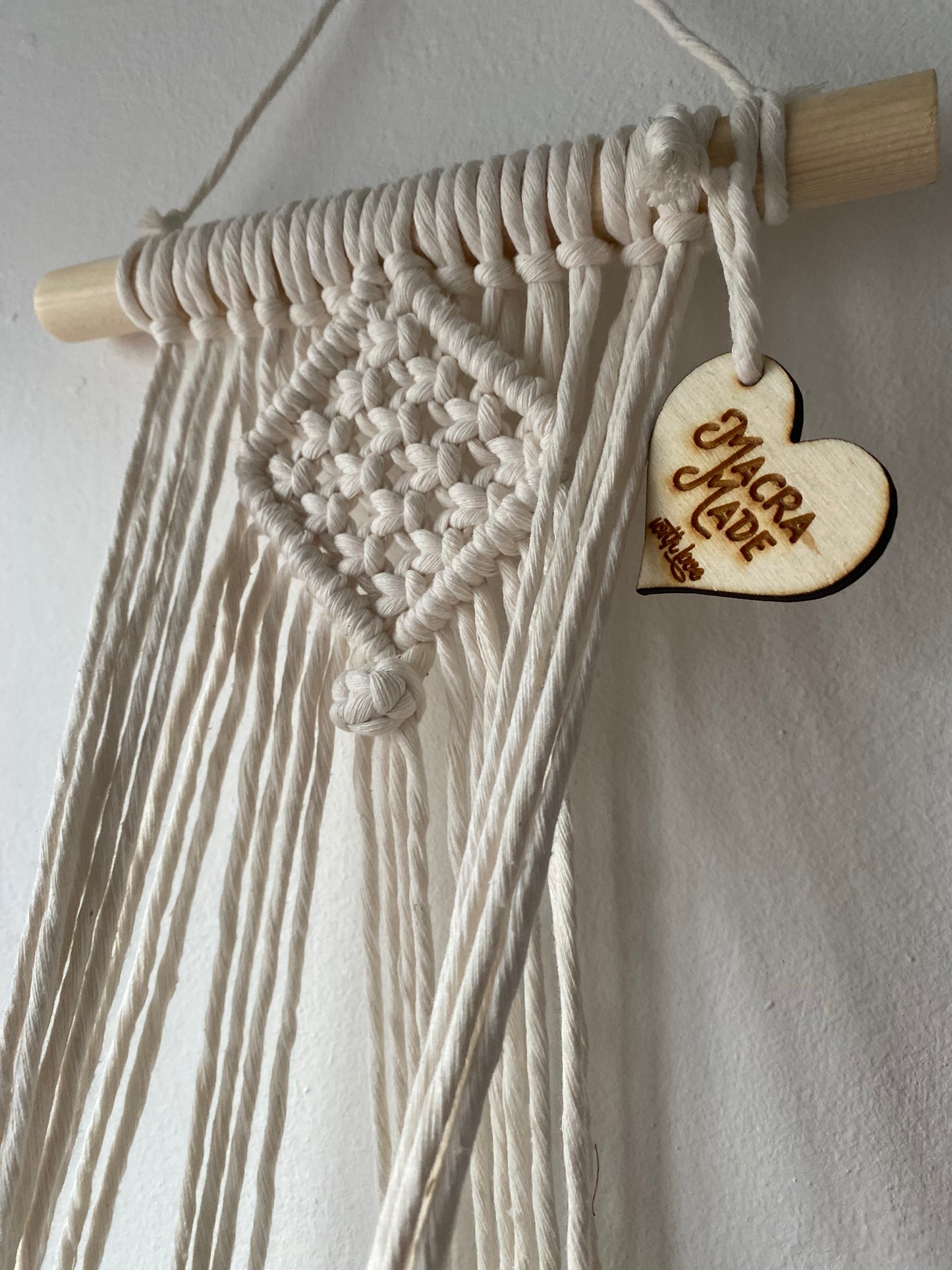 Close up of the intricate knots pattern on a handmade macrame plant holder, made with natural cotton on a pale wood dowel 