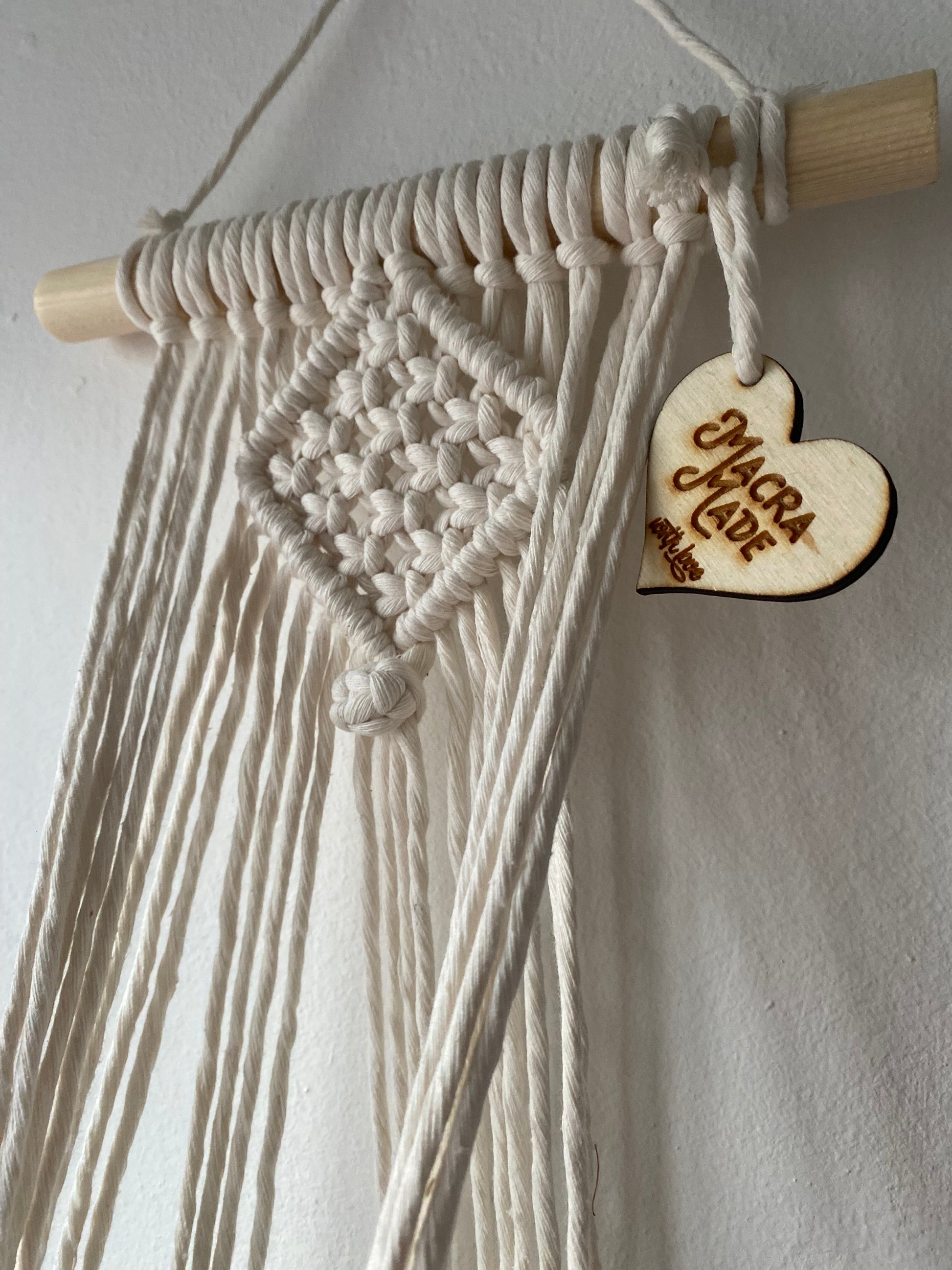 Close up of the intricate knots pattern on a handmade macrame plant holder, made with natural cotton on a pale wood dowel 