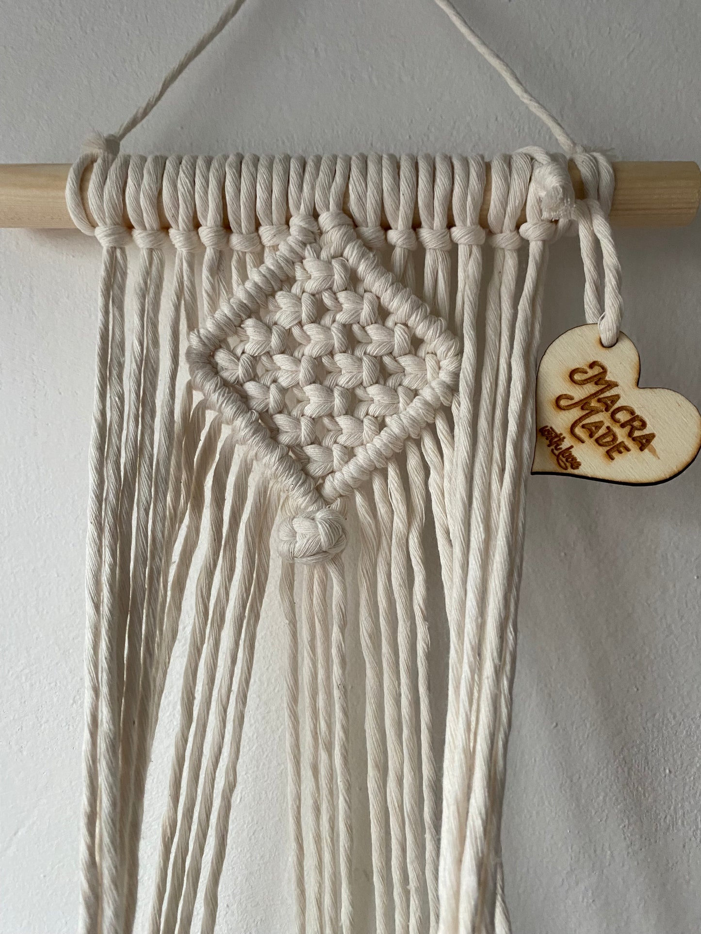 Close up of the top part of a macrame plant holder, made with natural cotton on a pale wood dowel 