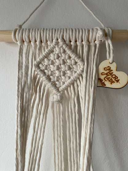 Close up of the top part of a macrame plant holder, made with natural cotton on a pale wood dowel 