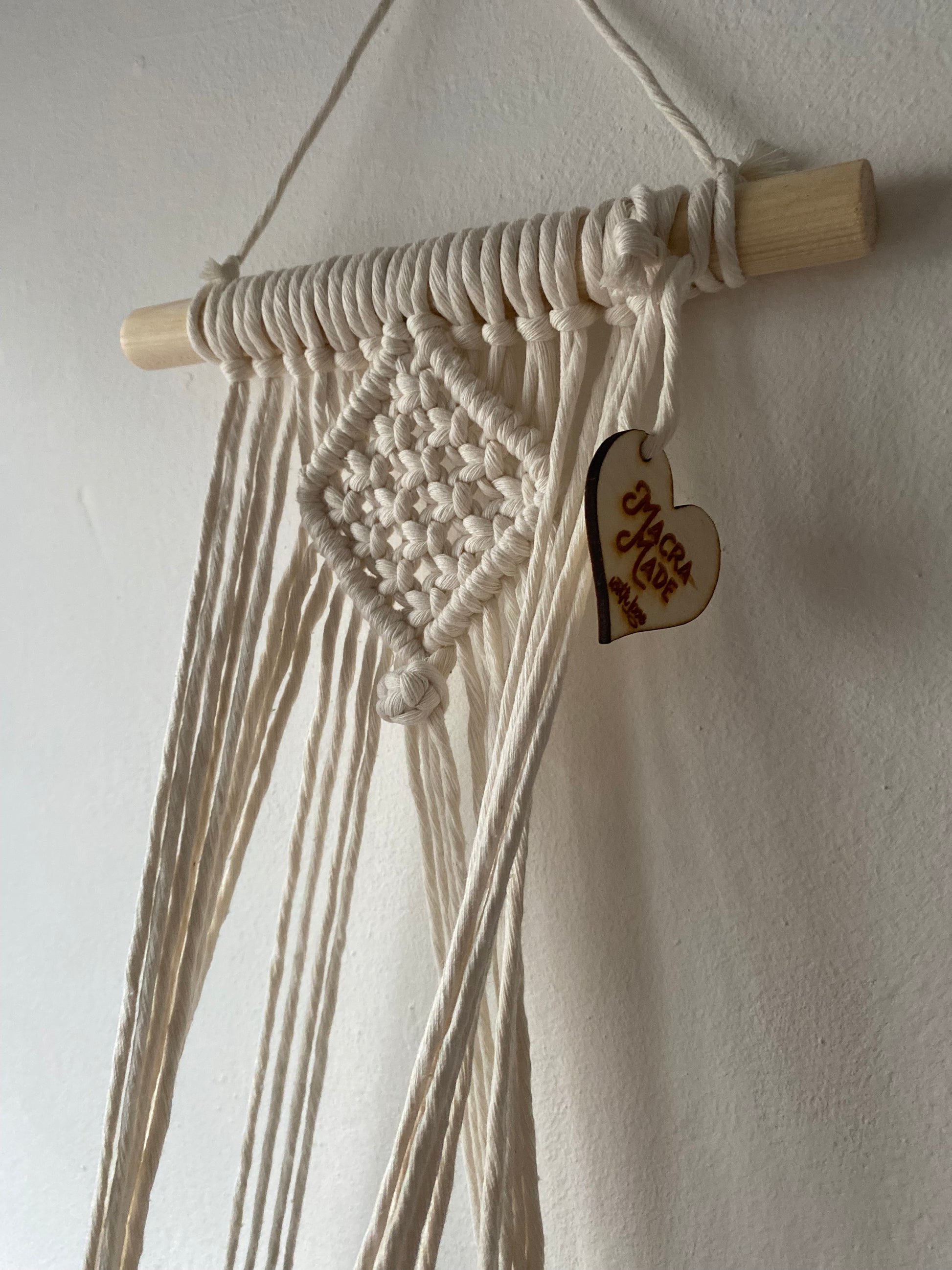 Close up of the top section of a macrame plant holder, made with natural cotton on a pale wood dowel 