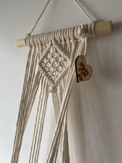 Close up of the top section of a macrame plant holder, made with natural cotton on a pale wood dowel 