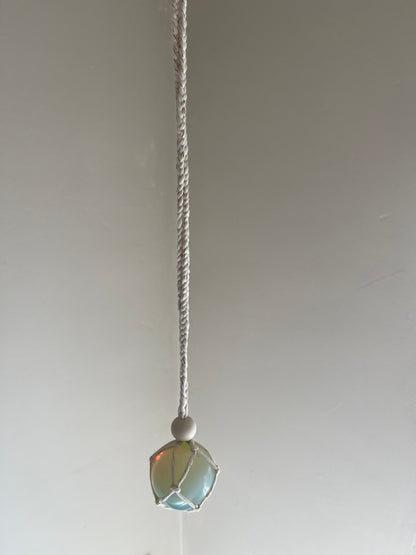 Handmade macrame opaline sphere hanging sun catcher, made with eco friendly natural recycled cotton yarn. The hanger is shown in front of a plain white wall, there is a plain wooden bead above the crystal.