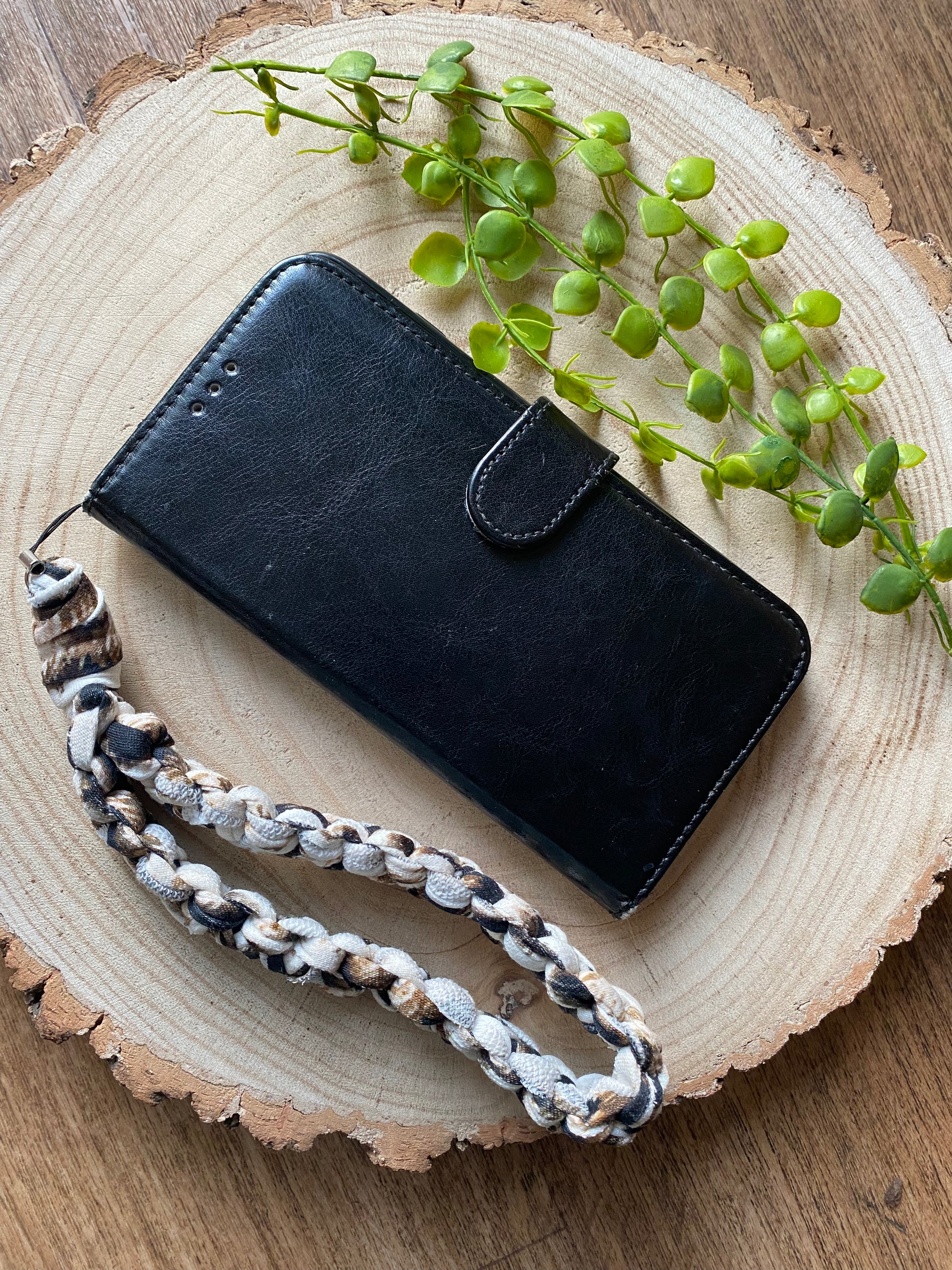 Handmade macrame phone wristlet strap in animal print recycled t shirt yarn, shown attached to a black leather wallet style phone case on a wooden surface. 