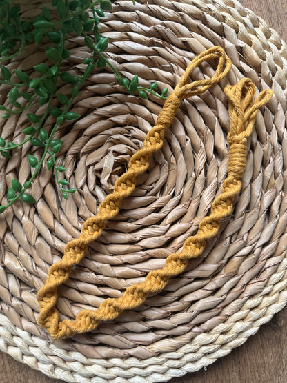Mustard yellow macrame plant hanger extension on a woven mat with greenery
